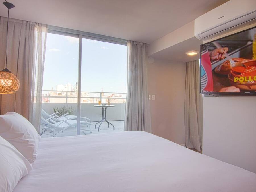 Ein Hotelzimmer mit Bett, Fernseher, einem Balkon mit Tisch und Stühlen sowie Blick auf die Stadt.