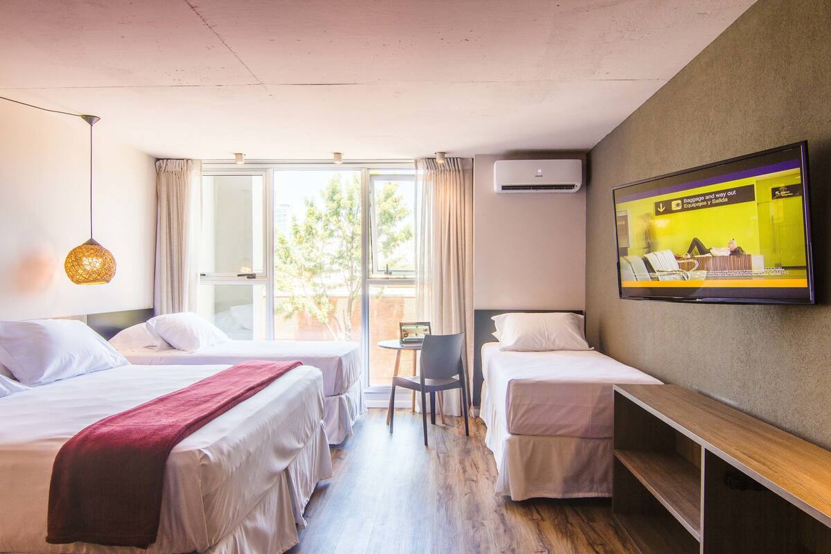 A hotel room with two beds, a TV, a desk, and a window with curtains.