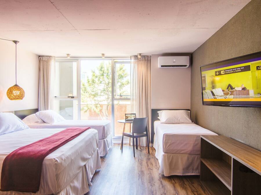 Habitación de hotel con dos camas, televisión, escritorio y ventana con cortinas.