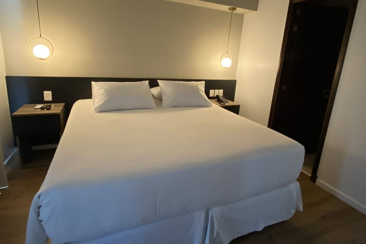 A neatly made bed with white bedding, two bedside tables with lamps, and a wooden floor.