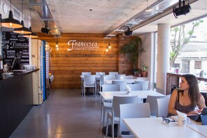 A café interior with wooden walls, white tables, and hanging lights. - Hotel Ciudadano Suites (Montevideo)