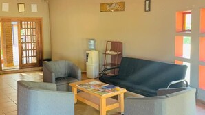 A living room with a thatched roof, a sofa, two armchairs, a coffee table, and a water dispenser. - Echo Lodge (Kang)
