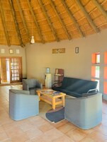Una sala de estar con techo de paja, un sofá, dos sillones, una mesa de centro y un dispensador de agua.