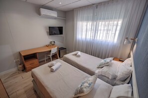 Habitación de hotel con dos camas, un escritorio, televisión y una ventana con cortinas.
