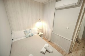 Et hotelværelse med en seng, et natbord, en lampe, et bruseområde og et håndklæde på gulvet.