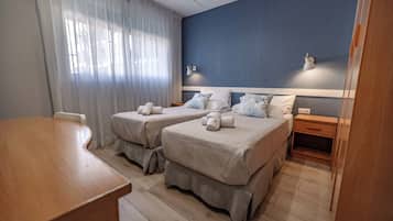 Ein Hotelzimmer mit zwei Betten, einem Holztisch, einem Nachttisch und einem Fenster mit Vorhängen.