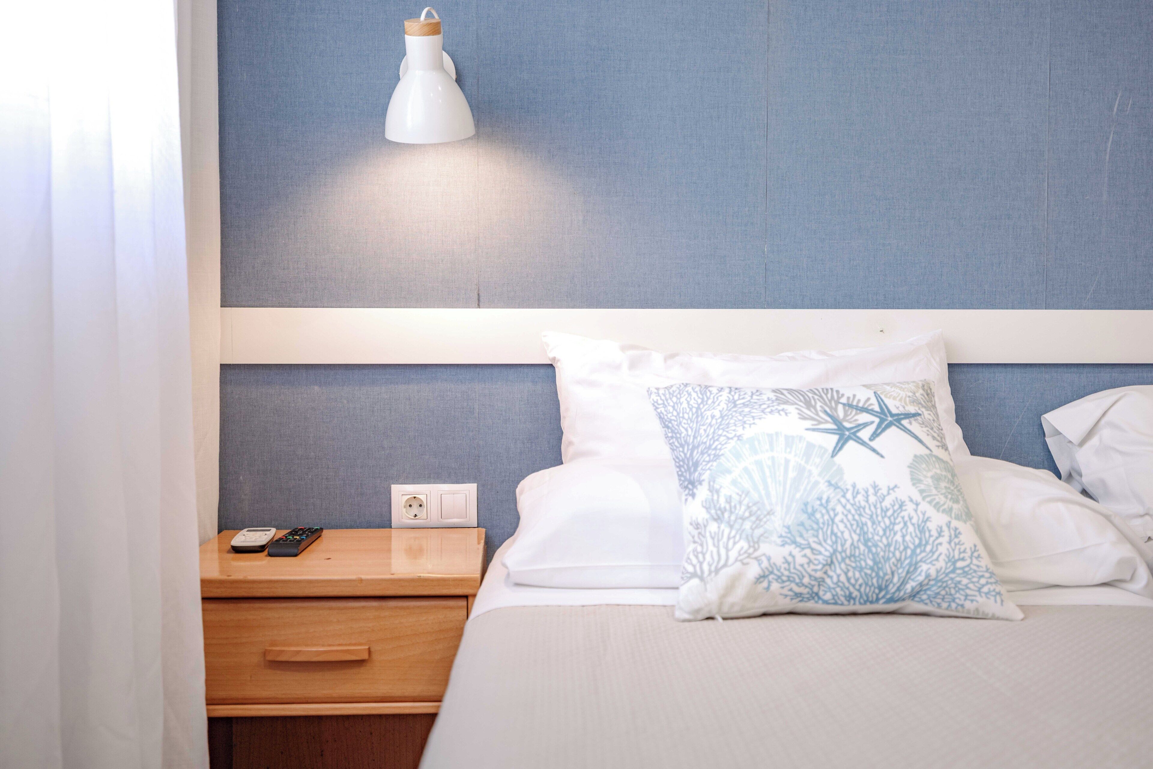 A hotel room with a bed, a nightstand, a lamp, and a power outlet.