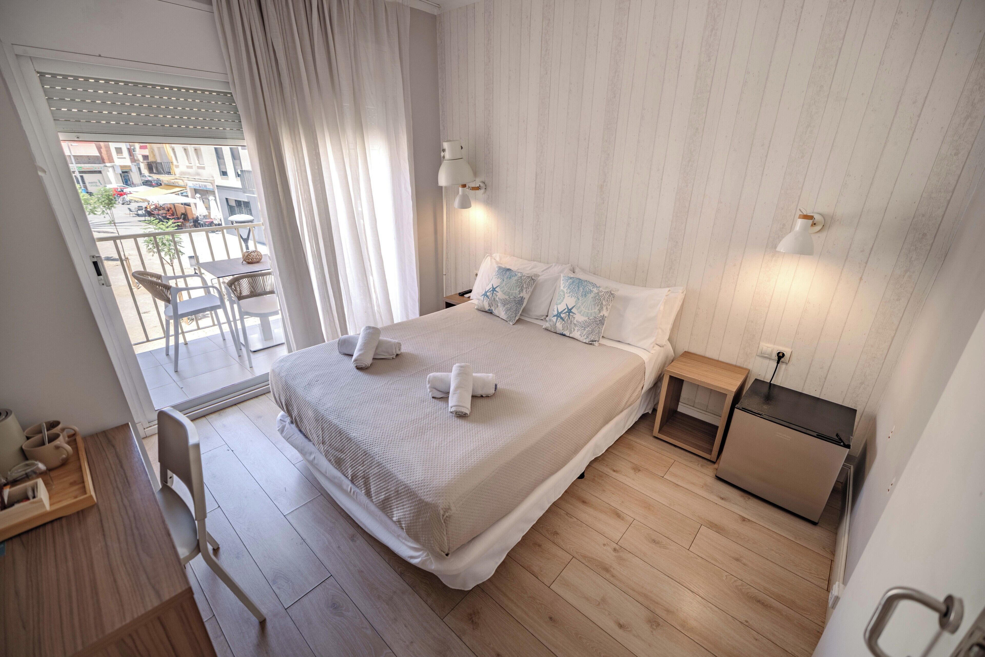 Habitación de hotel con una cama, dos mesitas de noche, un refrigerador pequeño y vistas al exterior.