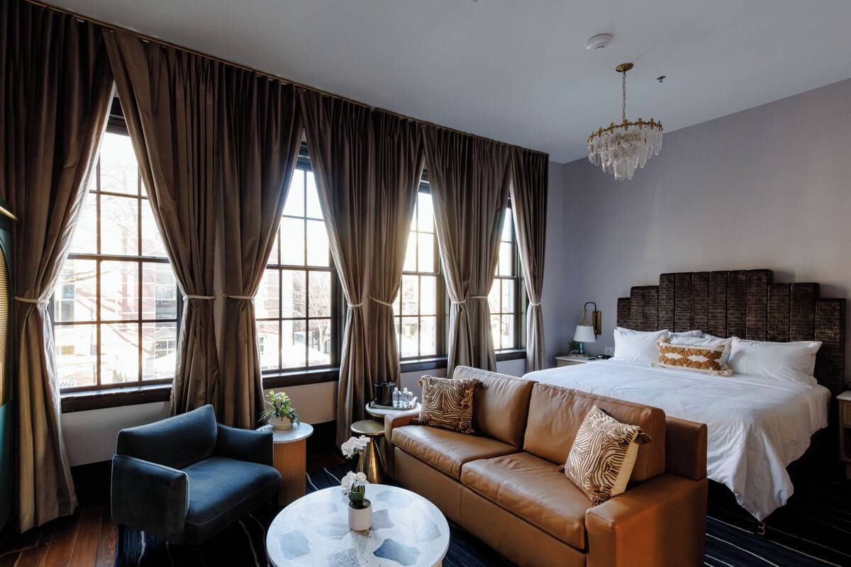 A hotel room with a large bed, a leather sofa, a round coffee table, and a chandelier.