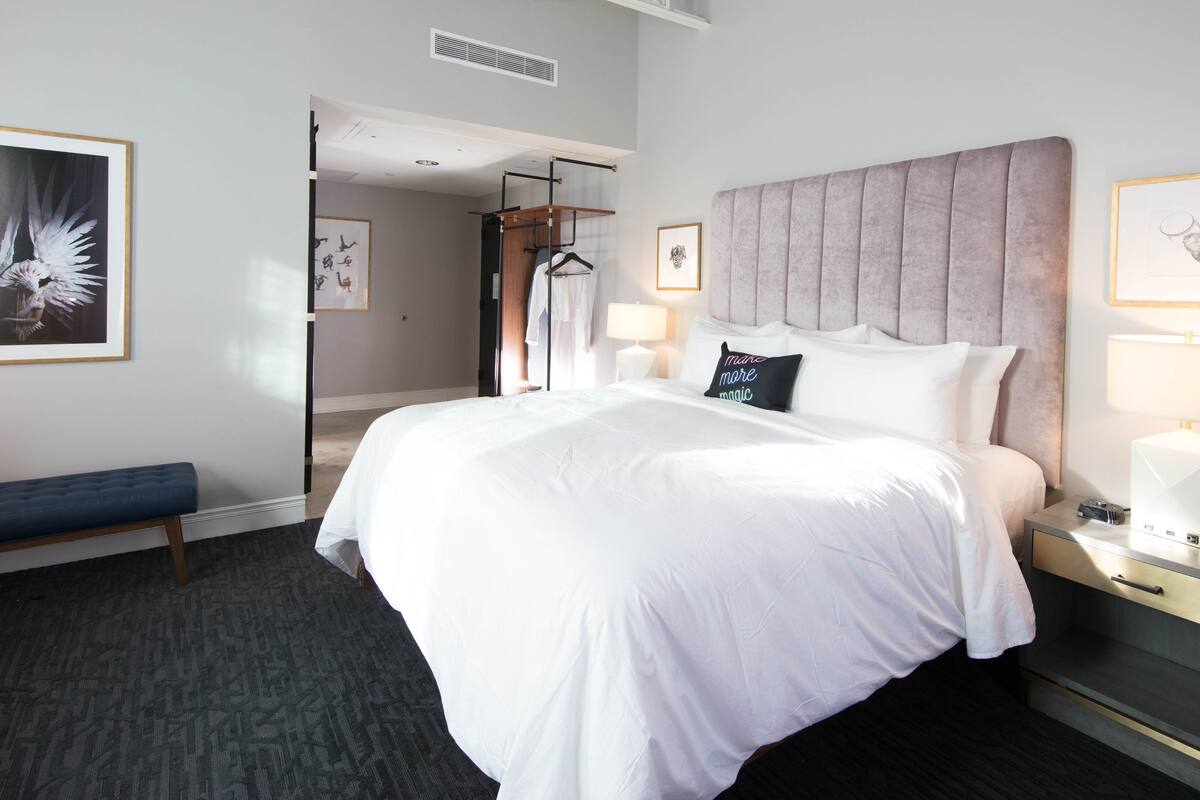 A hotel room with a large bed, bedside tables, a bench, and artwork on the walls.