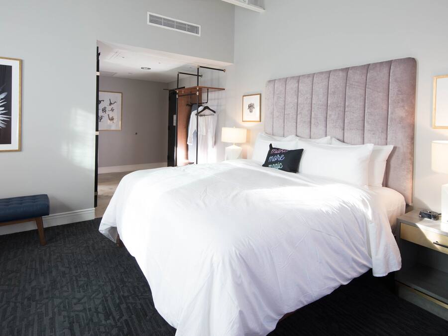 A hotel room with a large bed, bedside tables, a bench, and artwork on the walls.