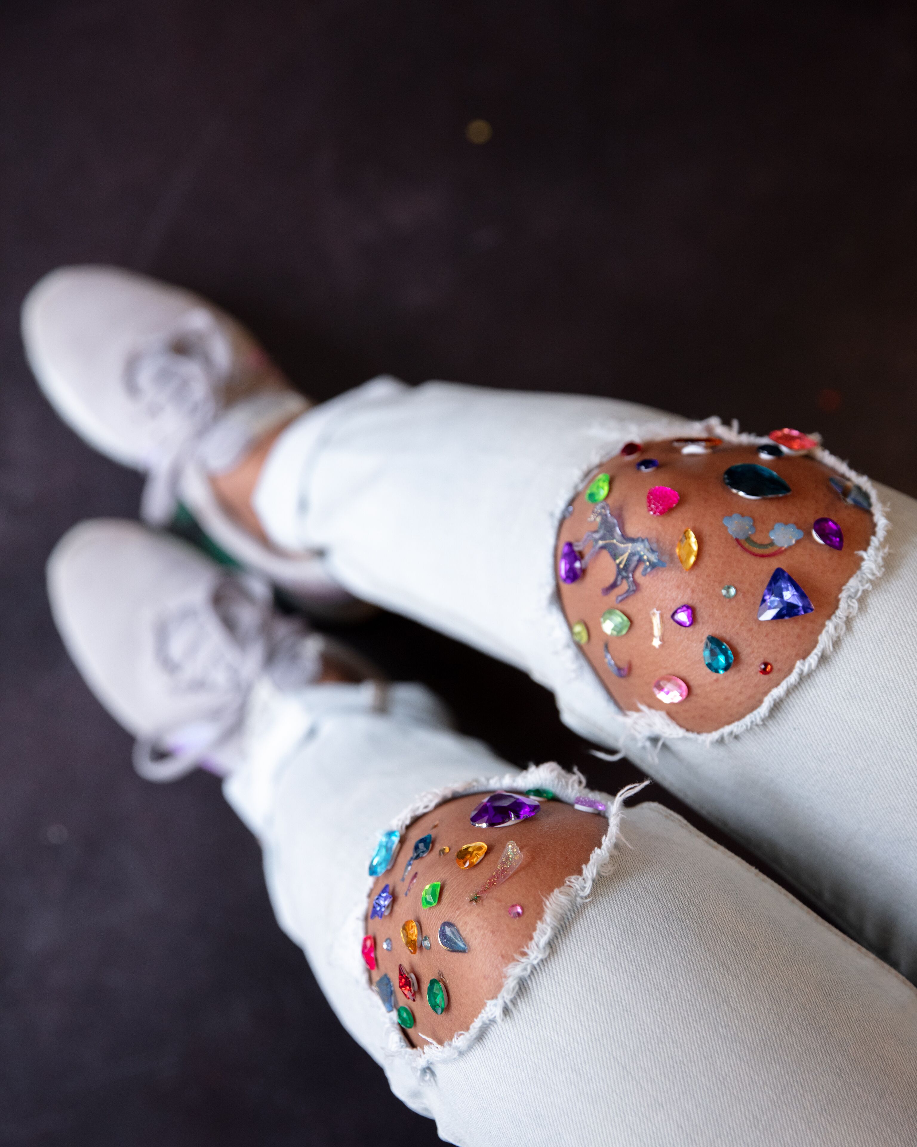 A pair of jeans with colorful embellishments and a white lace-up shoe.