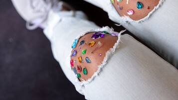 A pair of jeans with colorful embellishments and a white lace-up shoe.