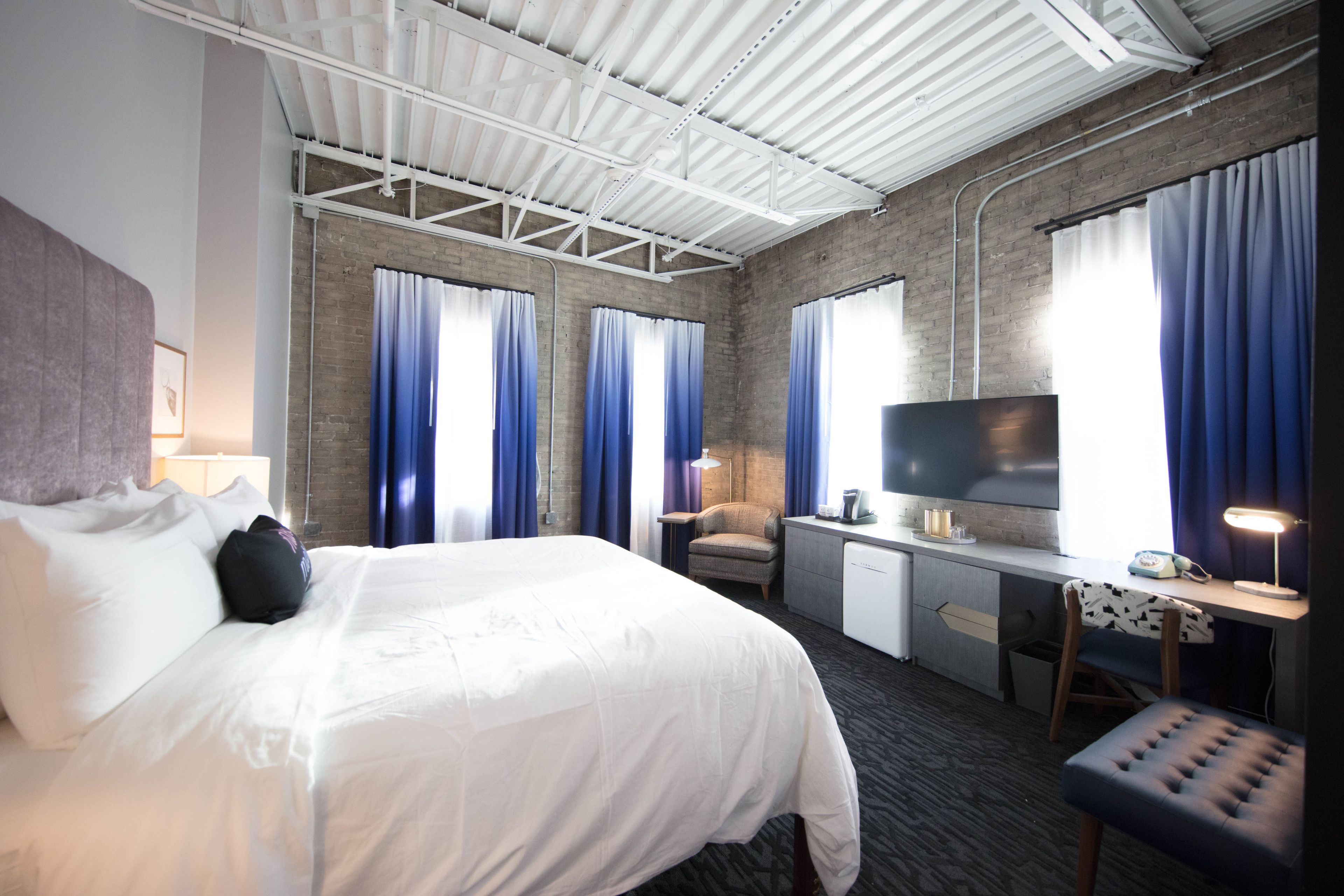 A hotel room with a bed, desk, chair, TV, and curtains.