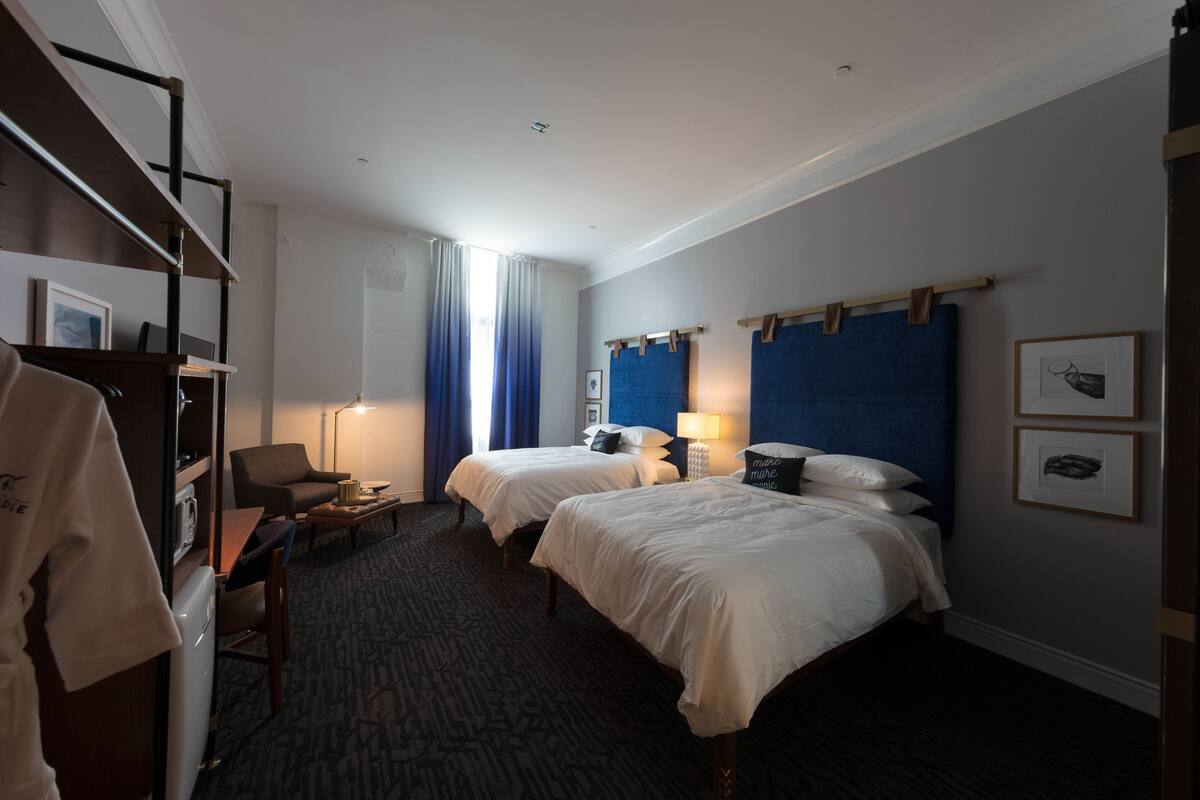 A hotel room with two beds, a desk, a chair, and a wardrobe.