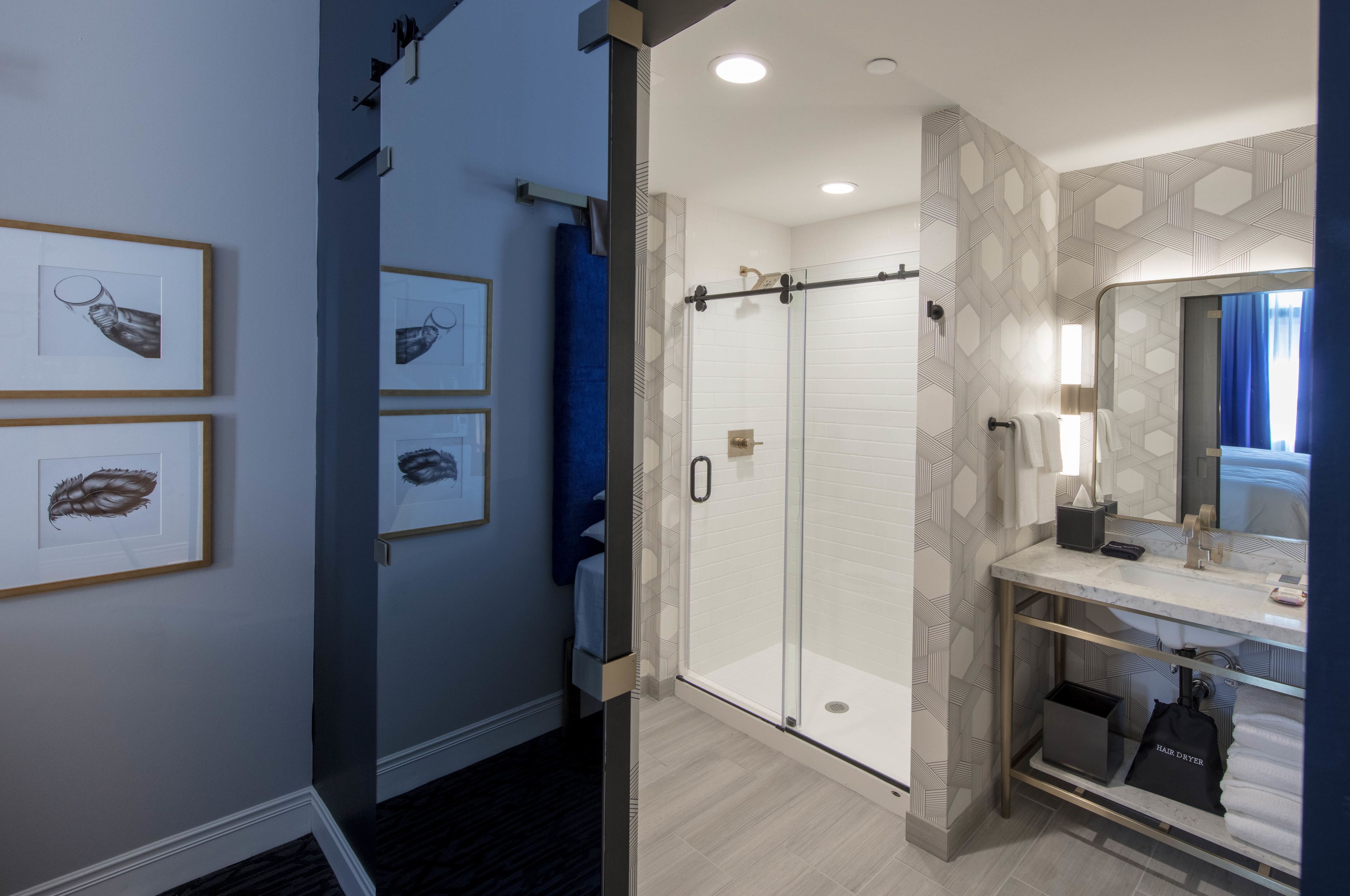 A modern bathroom with a glass shower enclosure, a vanity with a mirror, and framed artwork on the wall.