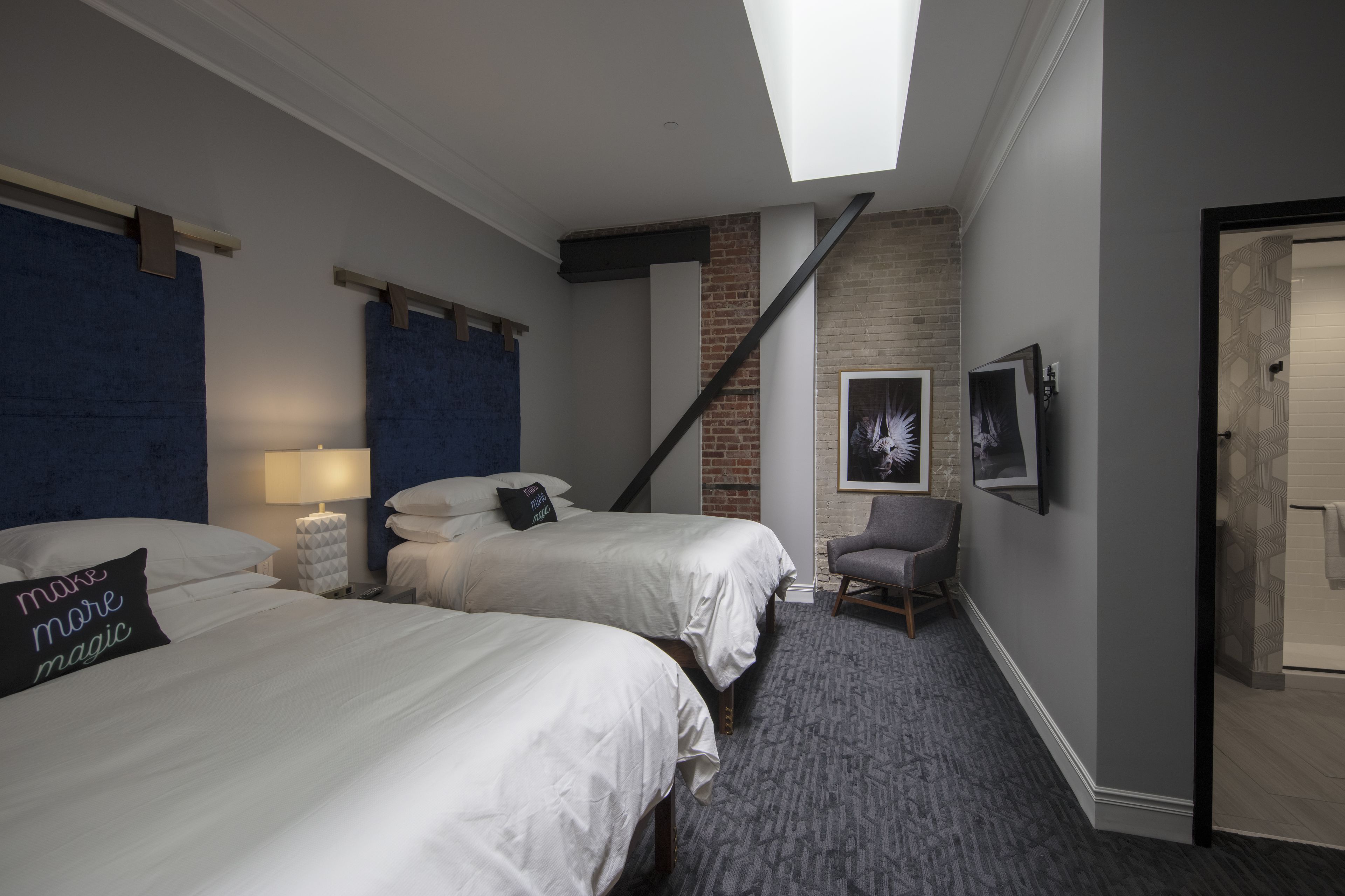 Ett hotellrum med två sängar, en stol, en lampa, en tavla och en trappa.