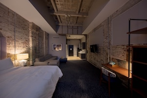 Camera d'albergo con pareti in mattoni a vista, un letto grande, una scrivania con telefono e una televisione appesa al muro.
