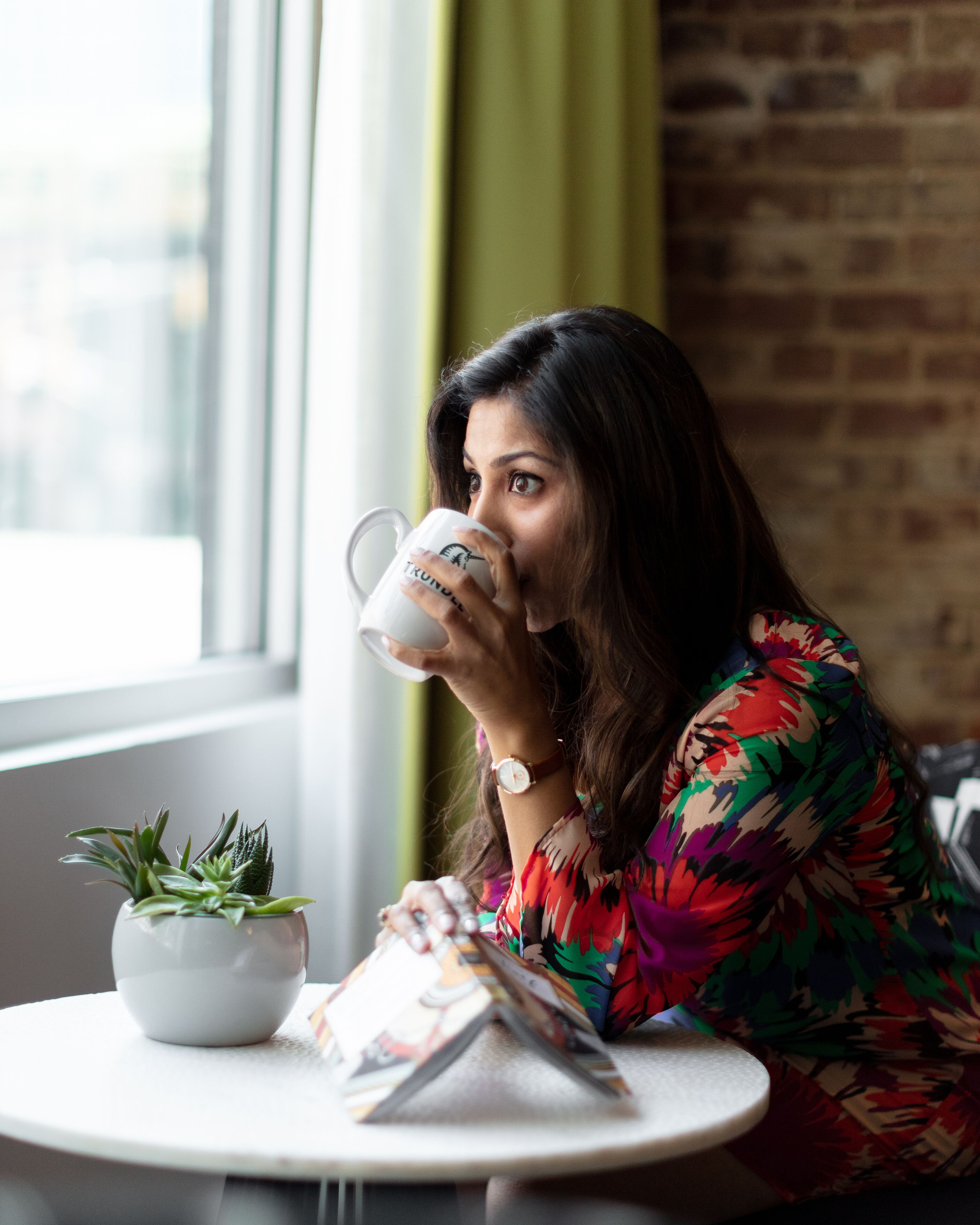 A person sitting at a table with a white mug, a plant, and a magazine.