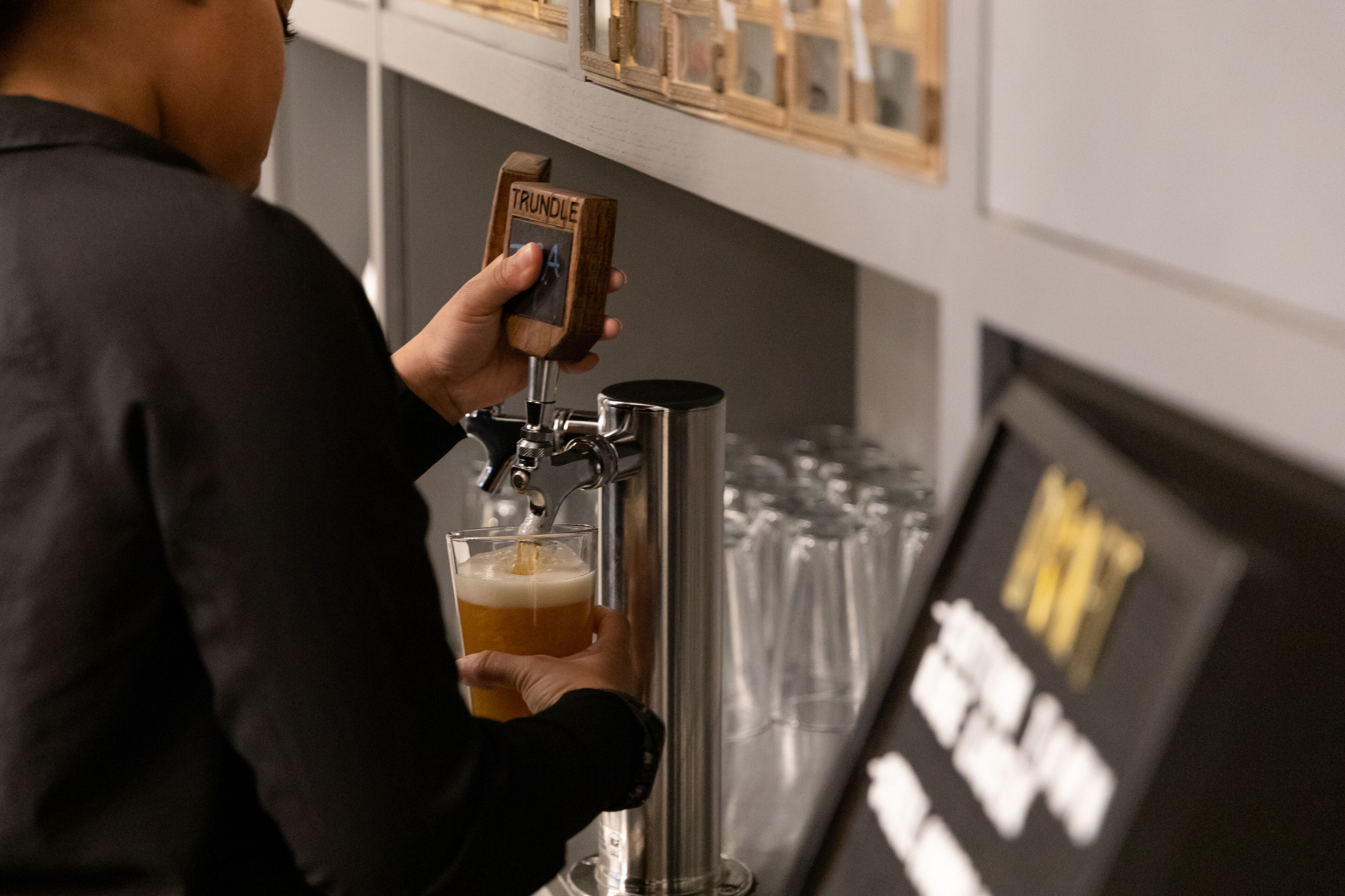 A person pouring beer from a tap labeled "TRUNDLE" into a glass.