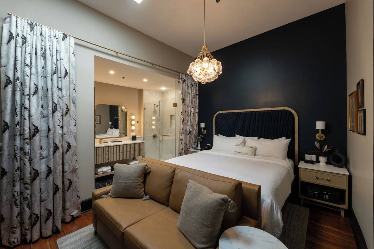 A modern bedroom with a large bed, a sofa, a bedside table, and a chandelier.