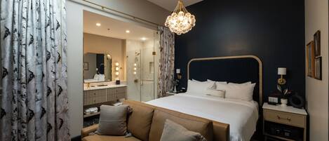 A modern bedroom with a large bed, a sofa, a bedside table, and a chandelier.