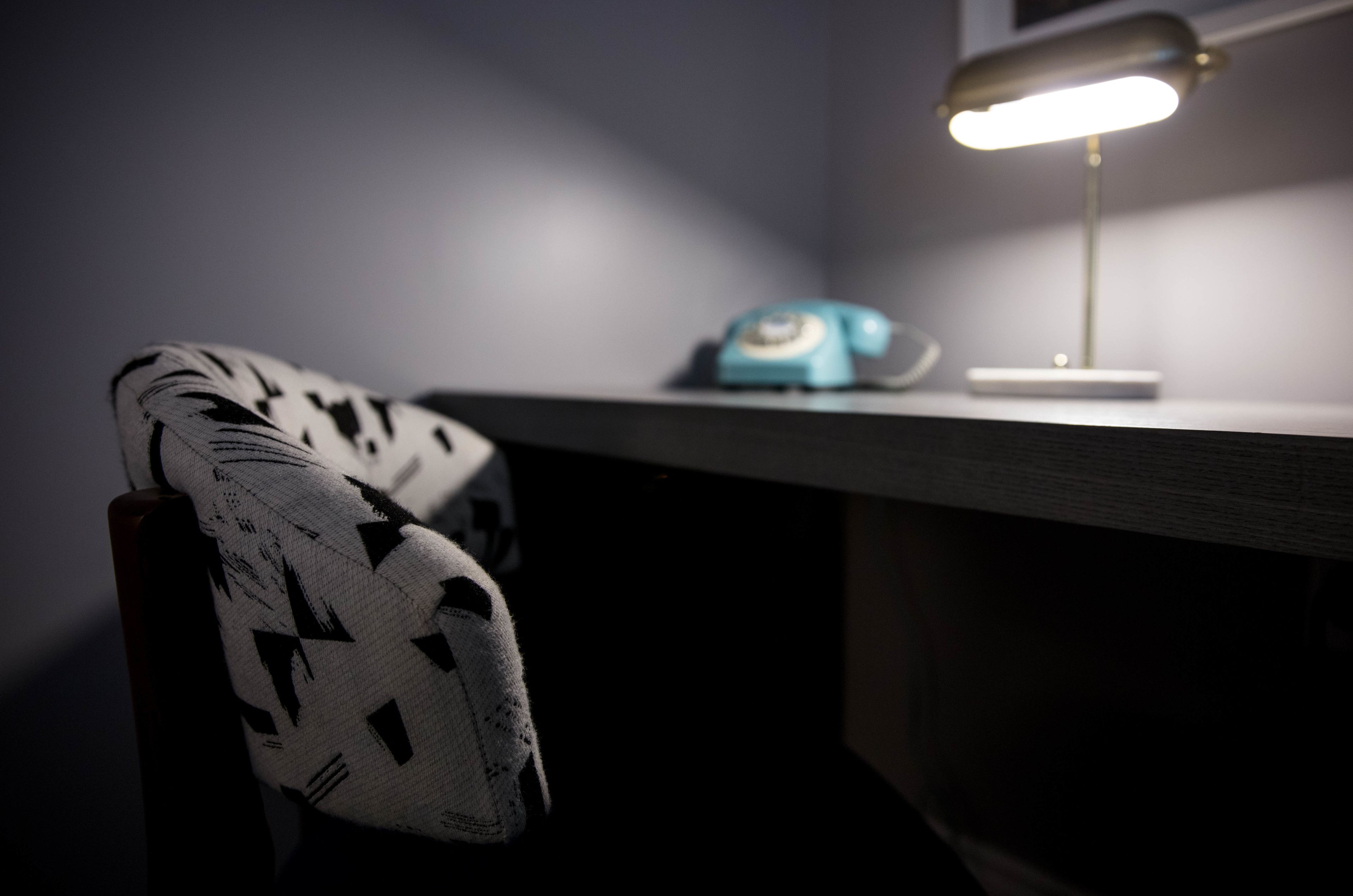 Una scrivania con una lampada, un telefono e una sedia con motivo decorativo.