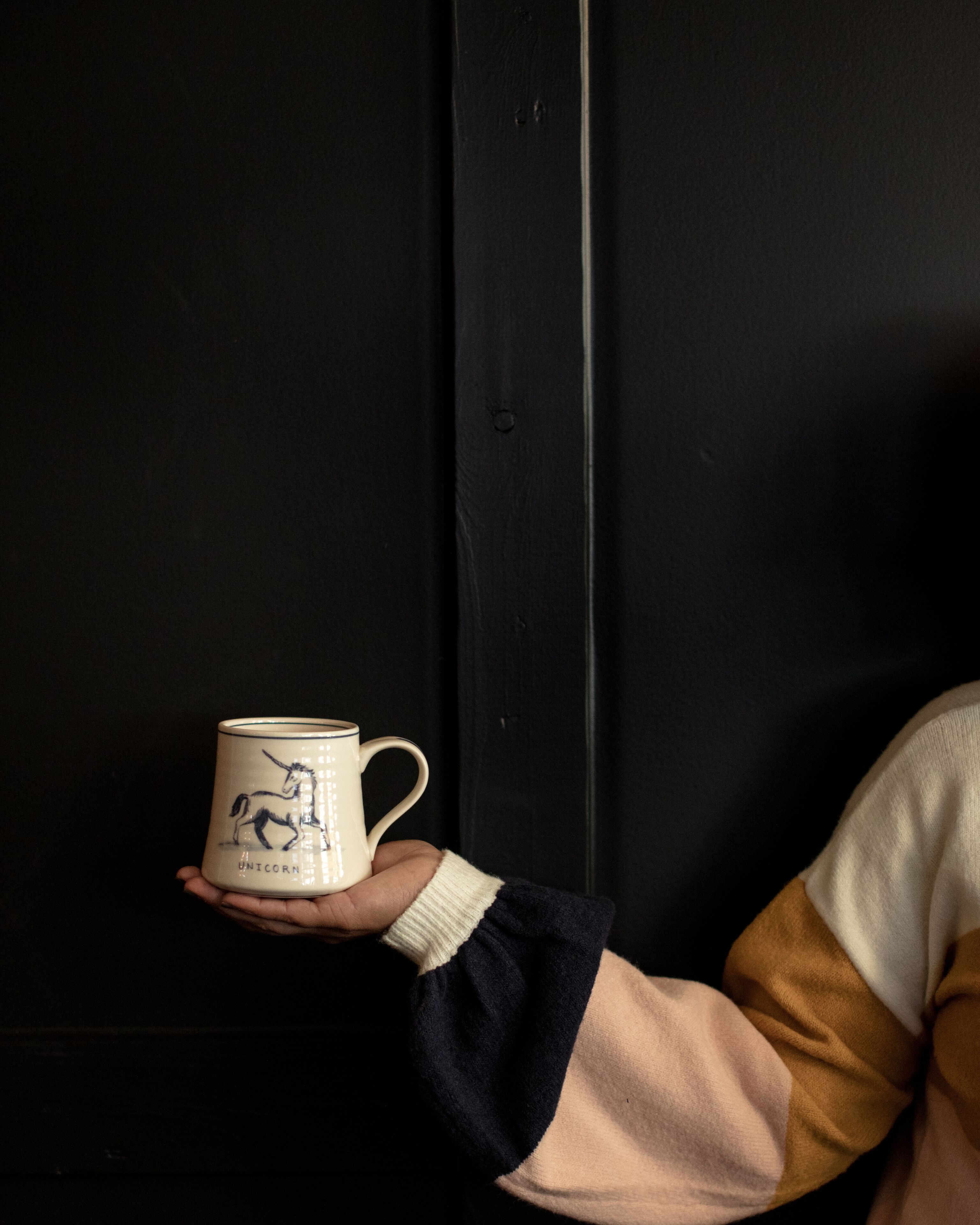 A hand holding a mug with a unicorn design against a dark background.