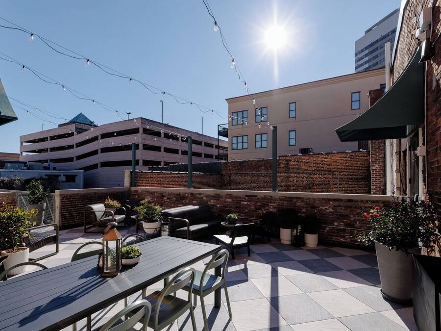 An outdoor patio area with a table and chairs, surrounded by potted plants and a brick wall.
