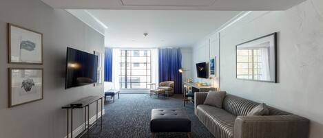 Ein Hotelzimmer mit großem Fenster, einer Couch, einem Fernseher und einem Schreibtisch.