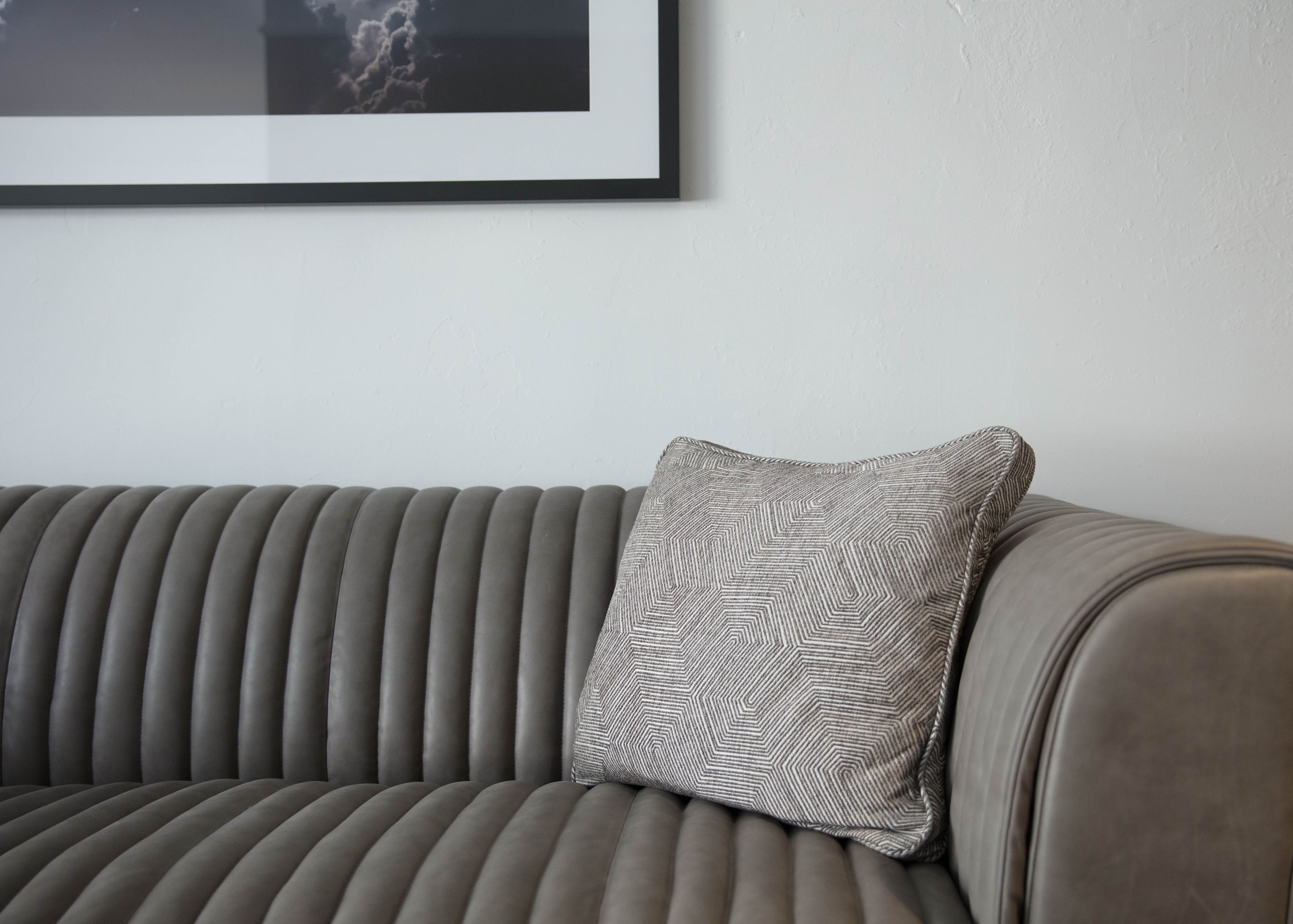 A grey upholstered sofa with a patterned pillow against a plain wall.