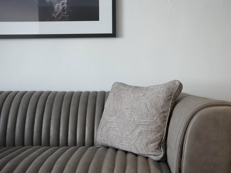 A grey upholstered sofa with a patterned pillow against a plain wall.