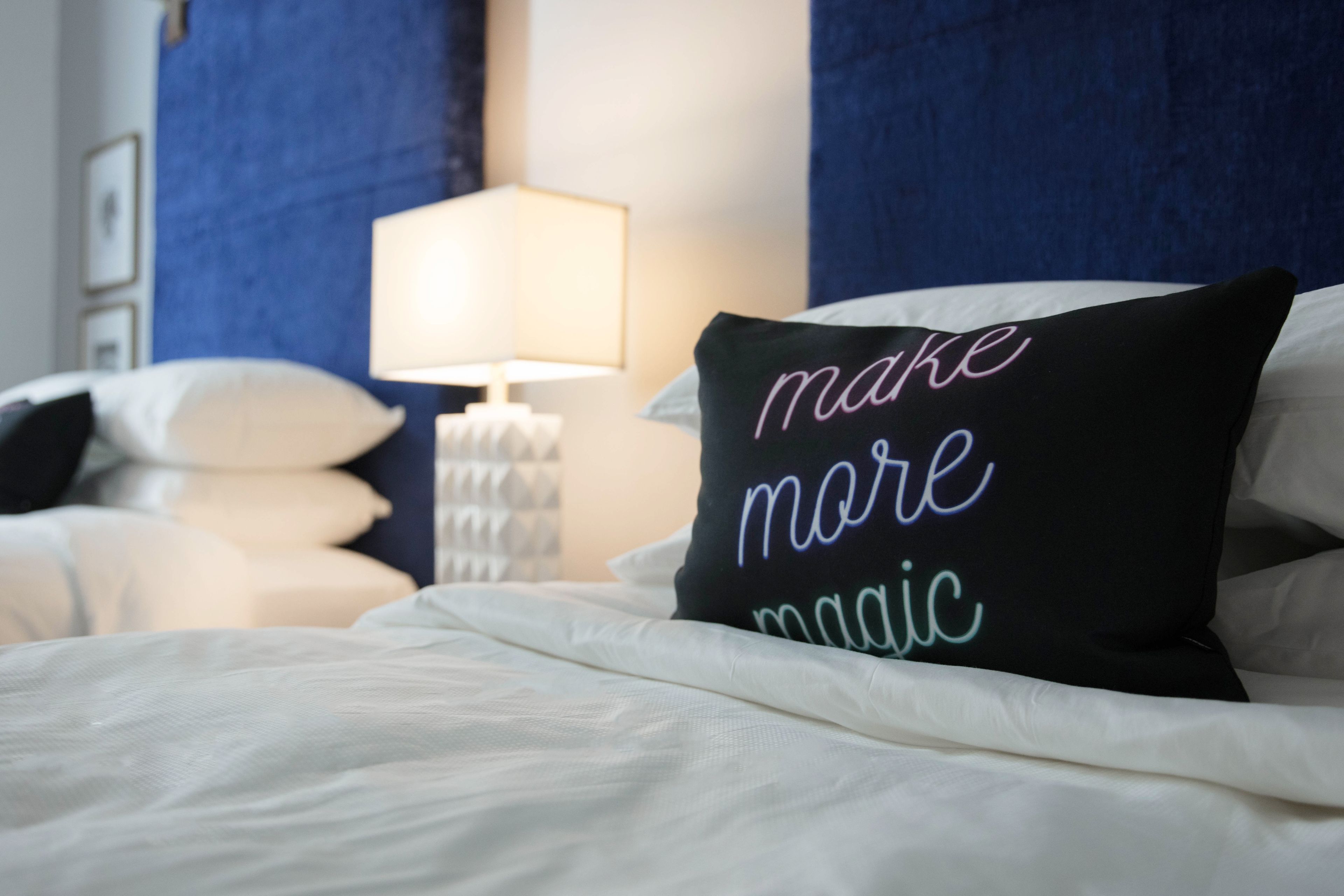 A neatly made bed with a pillow that reads "make more magic."
