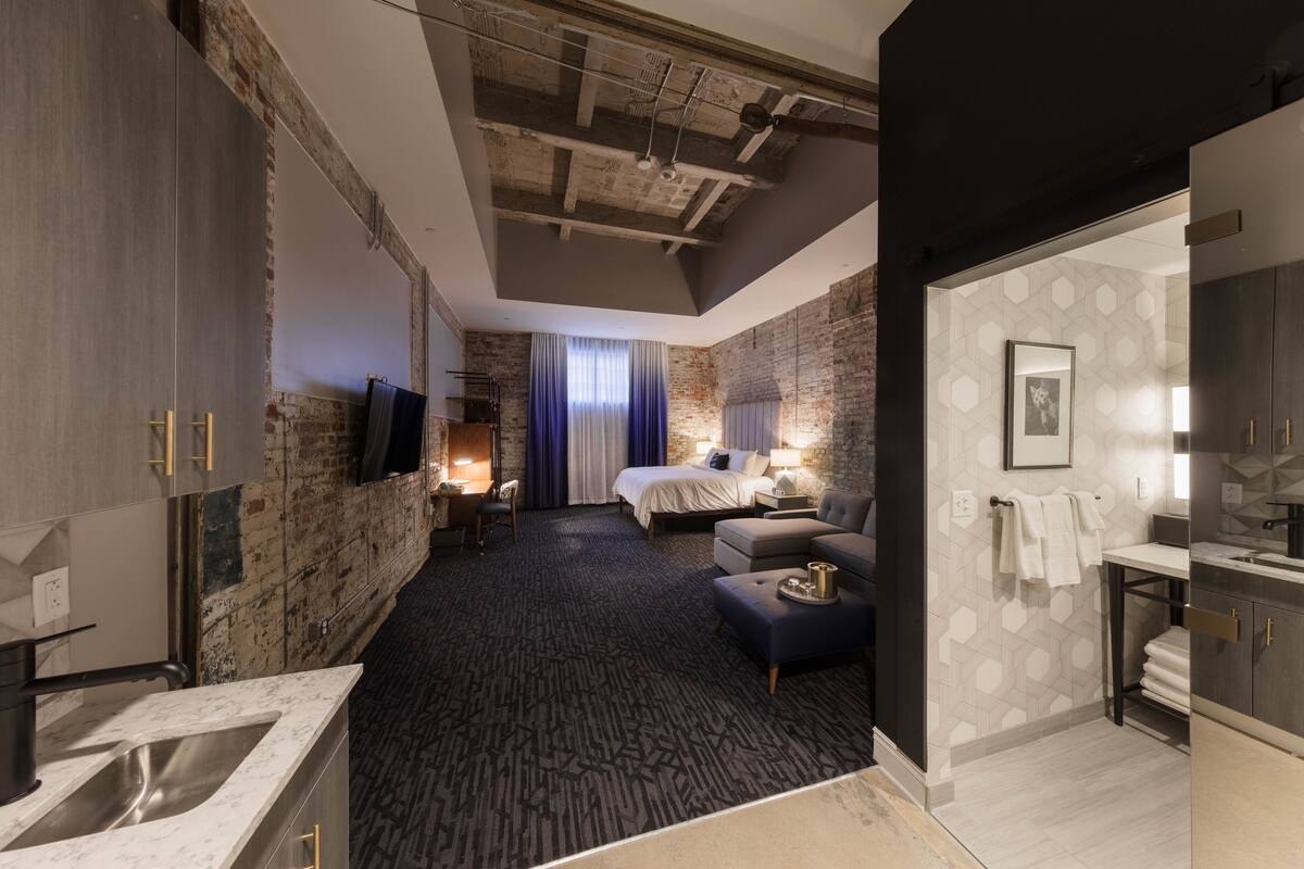 A modern hotel room with a large bed, a sofa, a desk, and a bathroom.