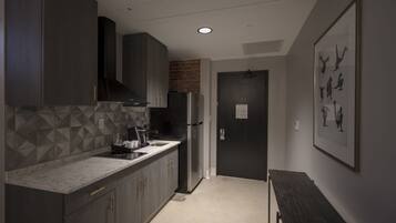 A modern kitchen with dark cabinets, a marble countertop, and a refrigerator.
