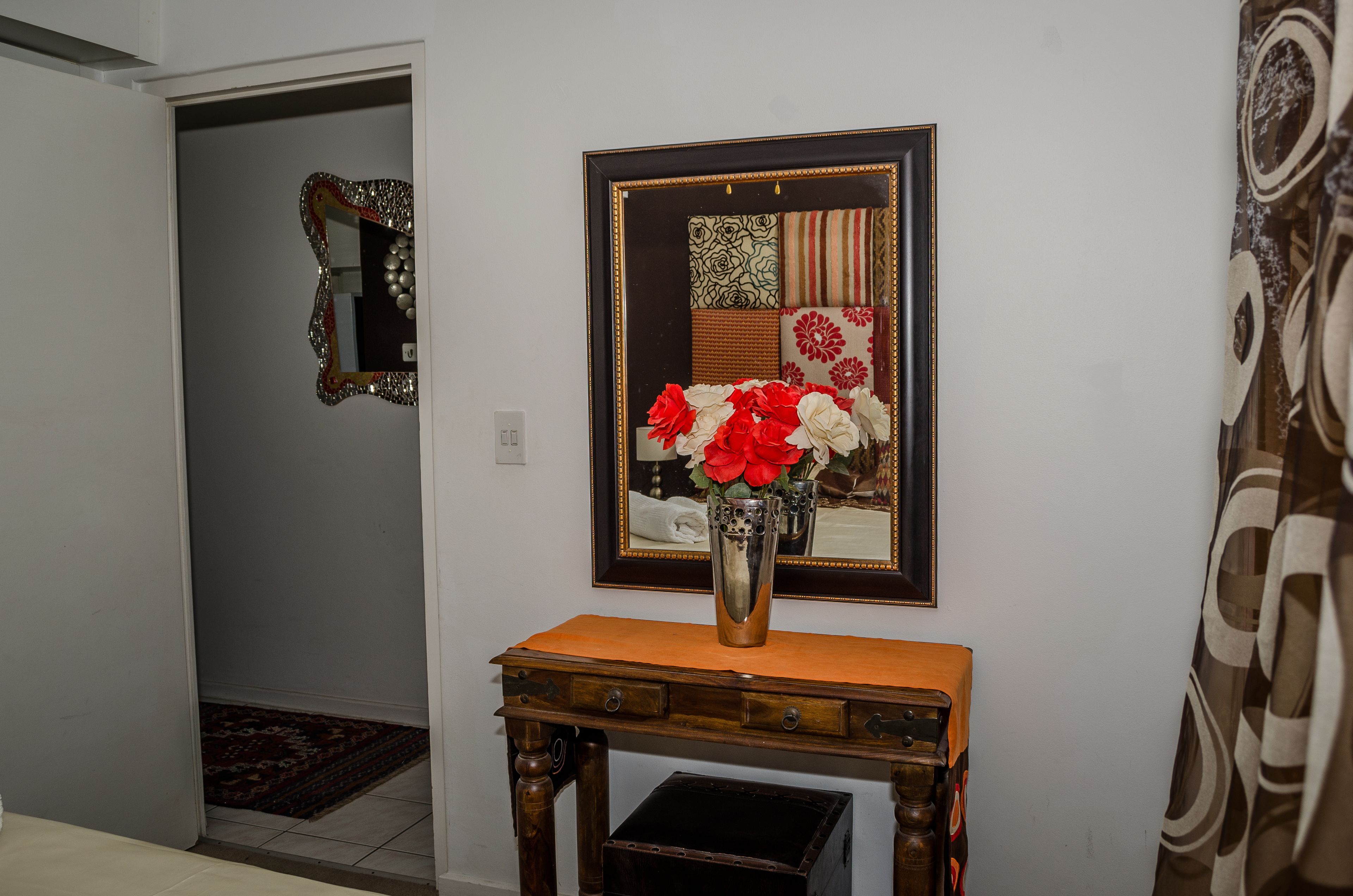 A hallway with a wooden console table, a mirror with a decorative frame, and a patterned curtain.