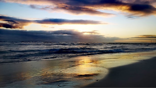 Ein Strand mit Wellen, Sonnenuntergang und bewölktem Himmel.