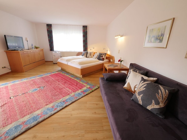 A bedroom with a bed, a sofa, a small table, a TV, a cabinet, and a window with curtains.