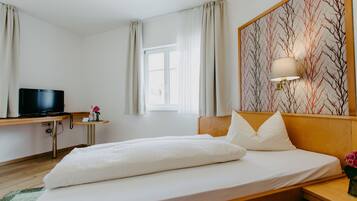 Ein Hotelzimmer mit Bett, Fernseher auf einem Schreibtisch, einem Fenster mit Vorhängen und einer Wand mit Baummuster.