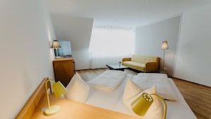 A modern hotel room with a sofa bed, a wooden side table, a desk with a lamp, and a large window with curtains. - Hotel Linde Durbach (Durbach)
