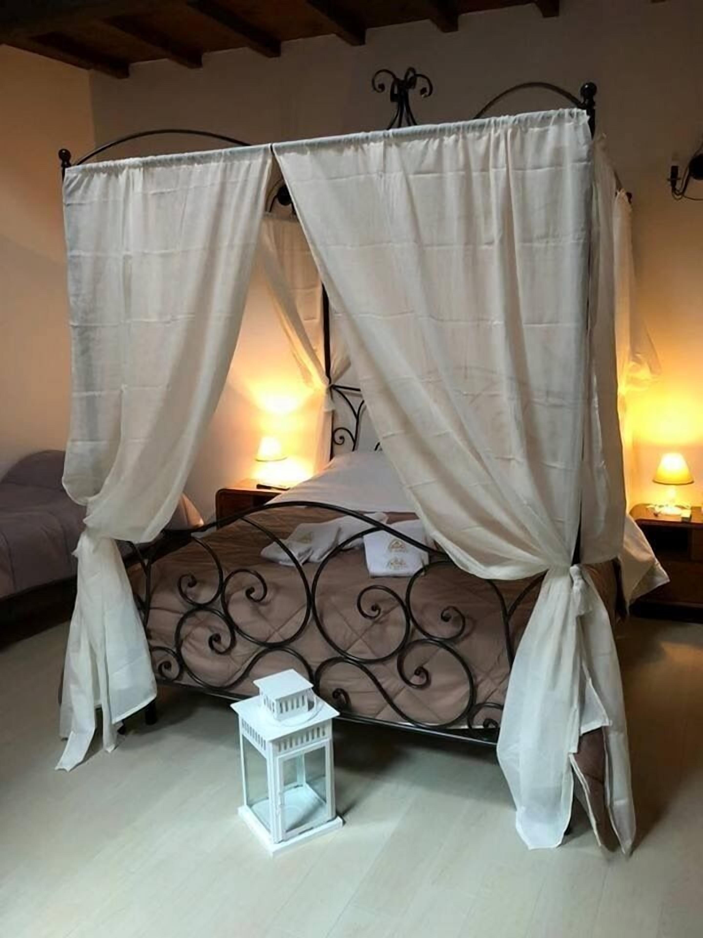 A four-poster canopy bed with a white canopy, a small white table lamp, and a decorative metal headboard.