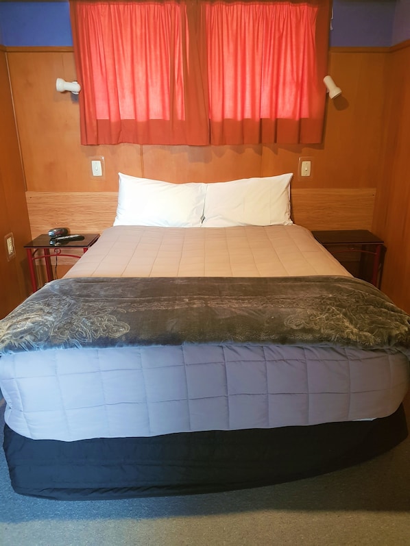 Une chambre d’hôtel avec un lit, une table de chevet, une lampe et un rideau rouge.