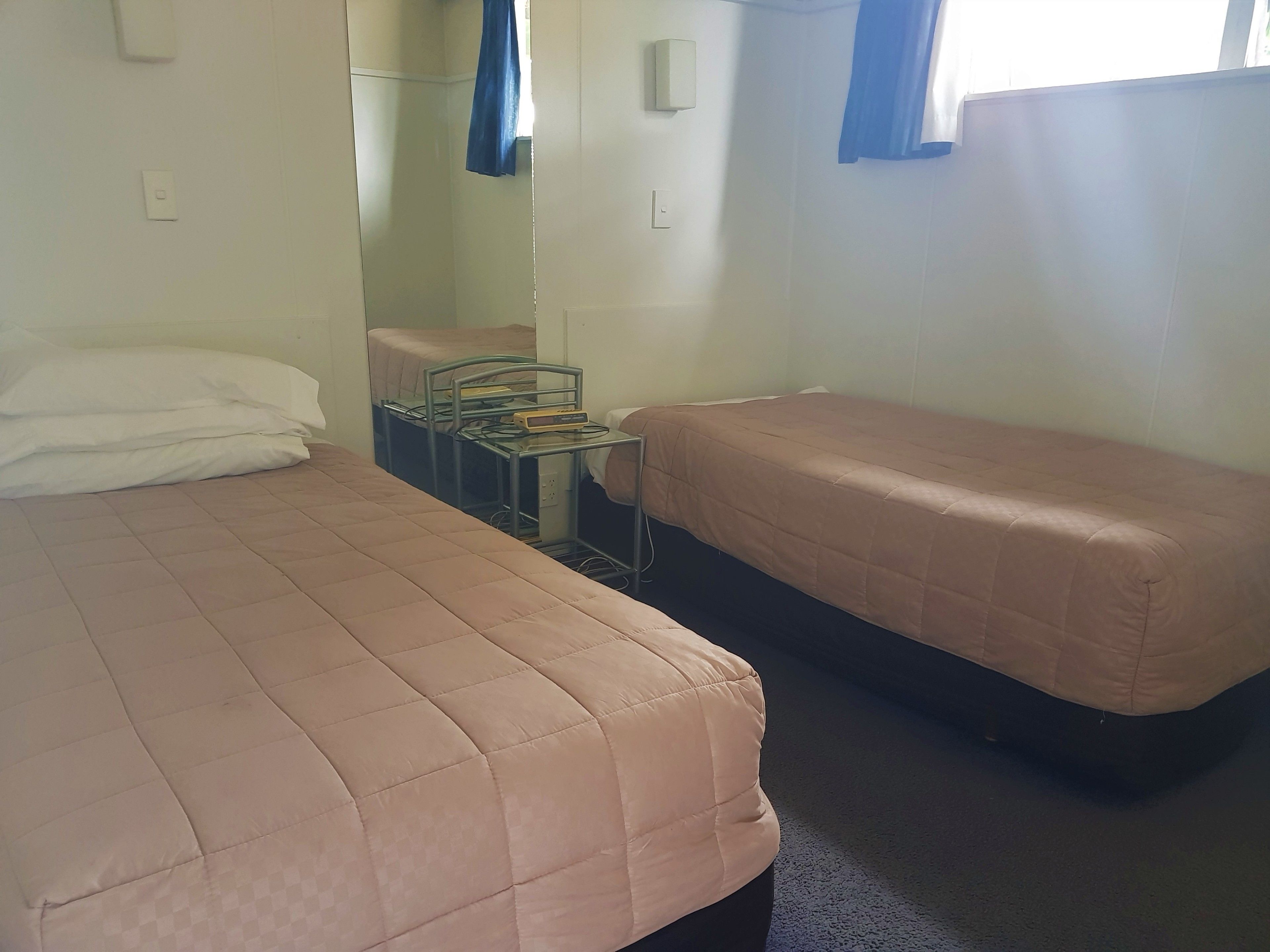 Una habitación con dos camas, una mesita con una computadora y una ventana con cortinas.