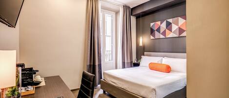 Une chambre d’hôtel moderne équipée d’un lit, d’un bureau avec une lampe, d’une télévision et d’une fenêtre avec des rideaux.