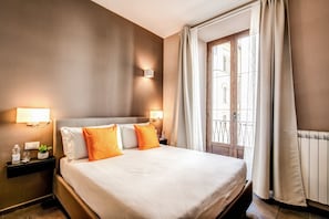 A hotel room with a large bed, two bedside lamps, a nightstand with a bottle and glasses, and a window with curtains. - H501 Luxury Rooms (Rome)