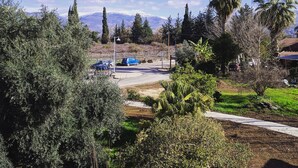 A residential area with a clear sky, a road with parked cars, and a mountain range in the background. - Al Sfat HaBanias (HaGalil HaElyon)