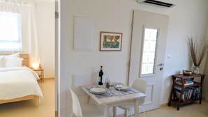 A hotel room with a bed, a dining table with chairs, a small table with a bottle and glasses, and a door with a window. - Al Sfat HaBanias (HaGalil HaElyon)