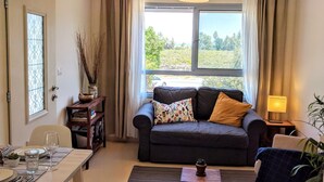 A living room with a sofa, a dining table set, a coffee table, and a window with curtains. - Al Sfat HaBanias (HaGalil HaElyon)