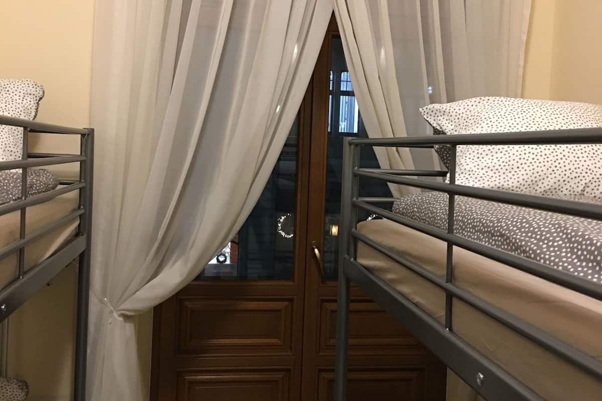 Quarto com beliches, porta de madeira e cortinas leves.
