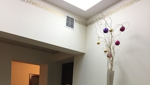 A room with a beige armchair, a wooden cabinet with glass doors, and a decorative vase with ornaments on the wall. - Ametyst Hostel (Kraków)